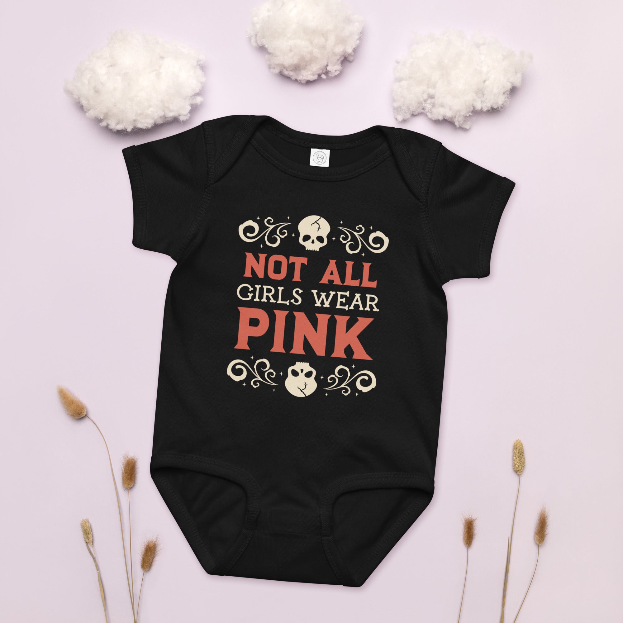 Black baby onesie with 'Not All Girls Wear Pink' text on a light pink background with decorative elements.