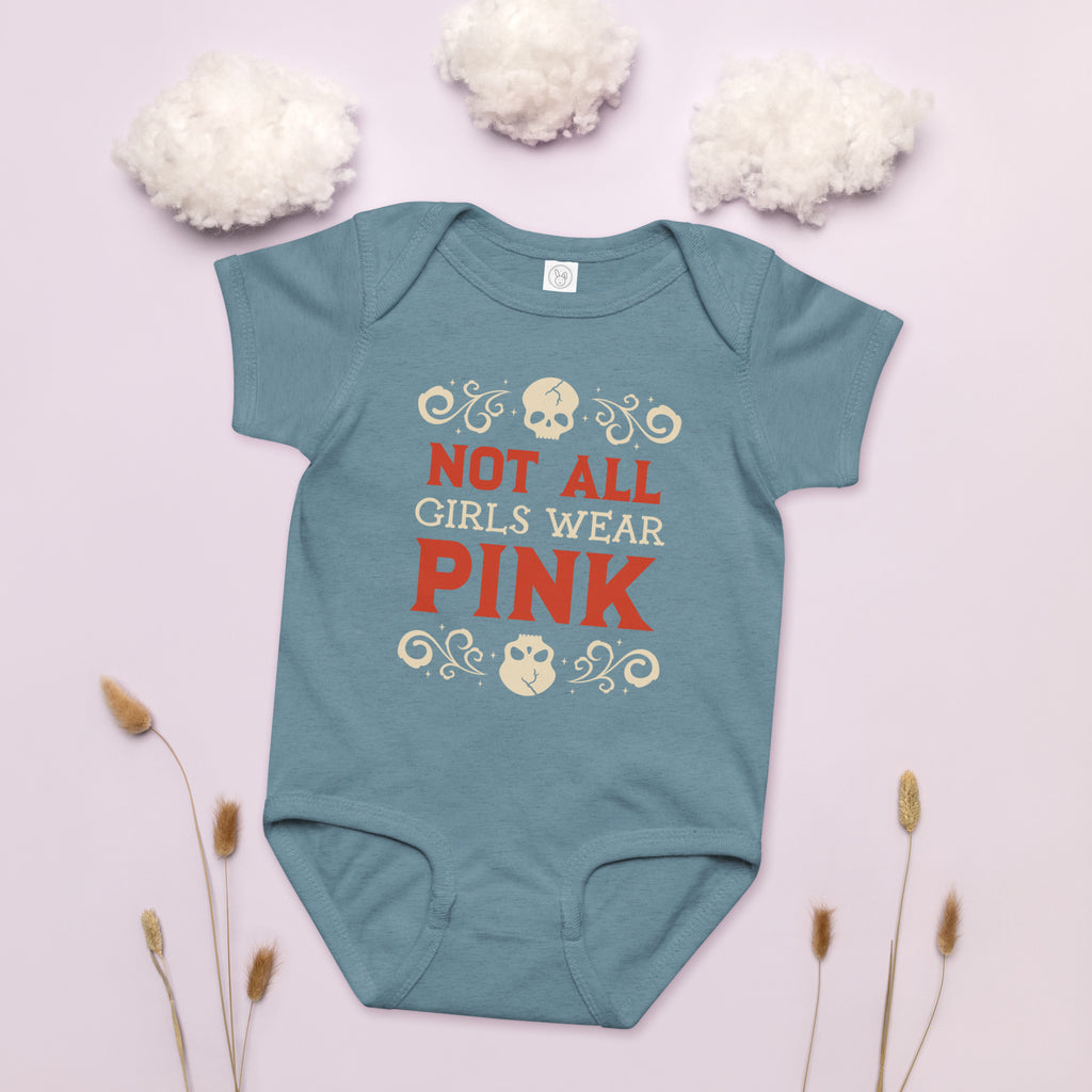 Teal baby onesie with 'Not All Girls Wear Pink' text on a light pink background with white flowers and dried plants.