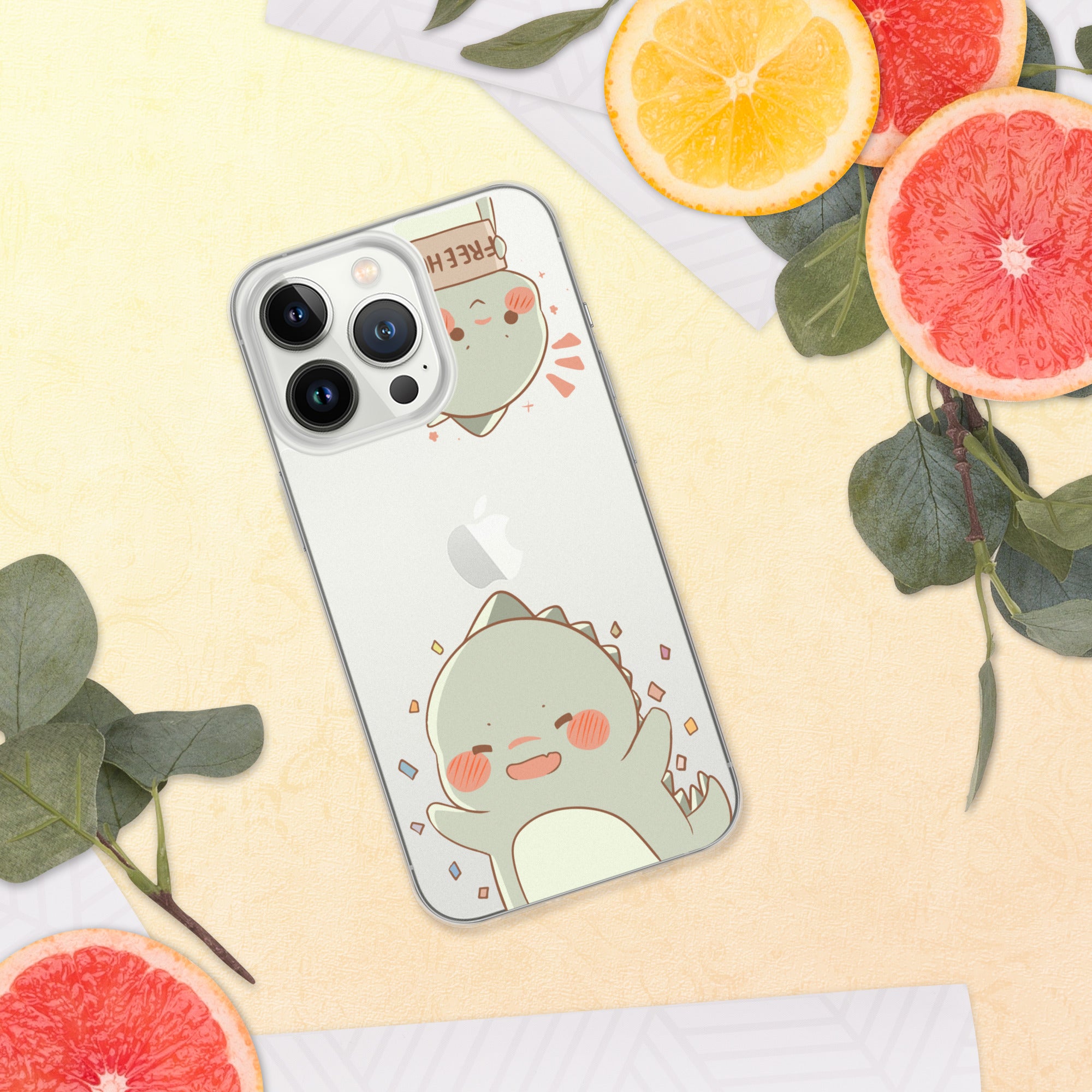 Phone case with a cute dinosaur design on a yellow surface with sliced oranges and leaves.