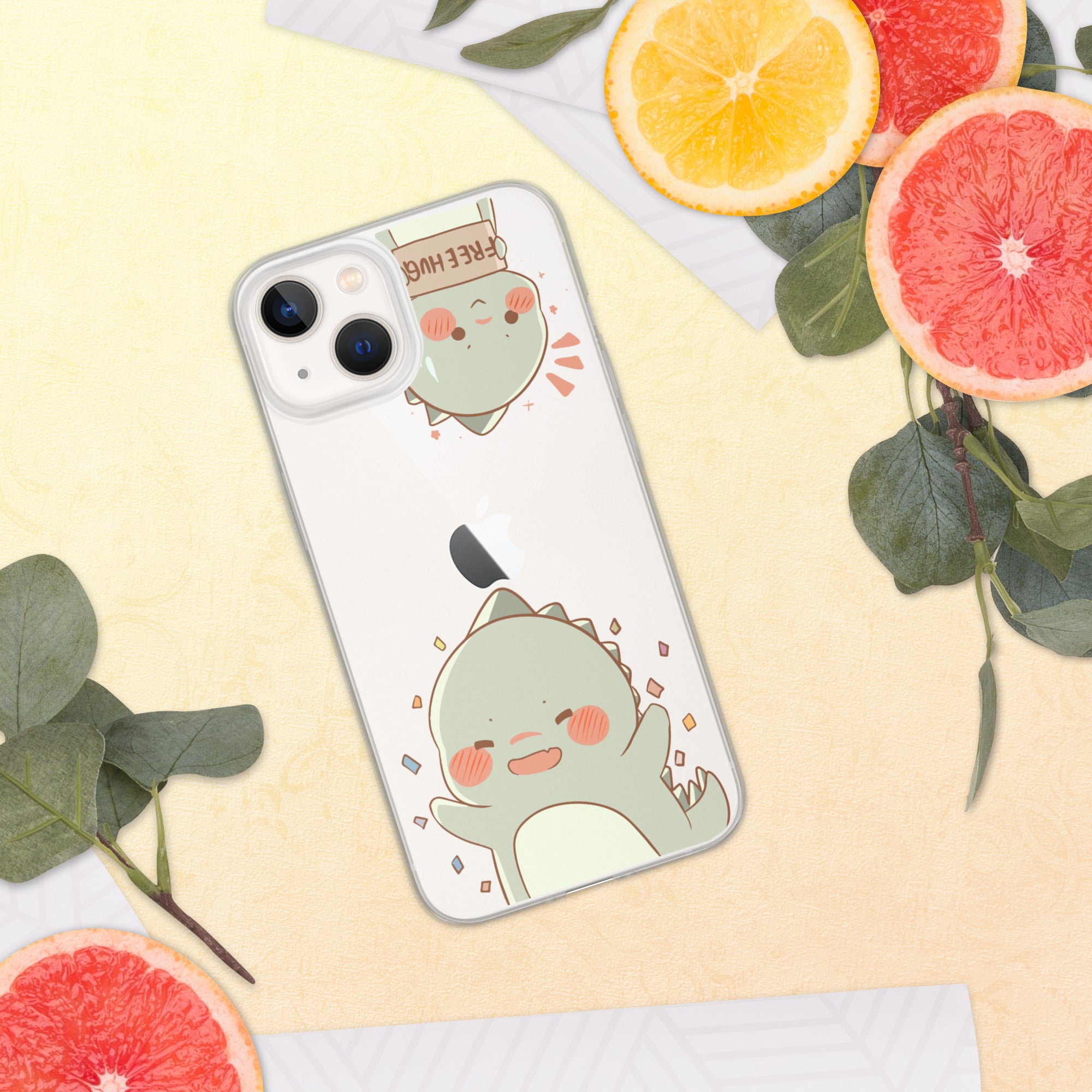 Phone case with a cute green dinosaur design on a yellow surface with fruit and leaves.