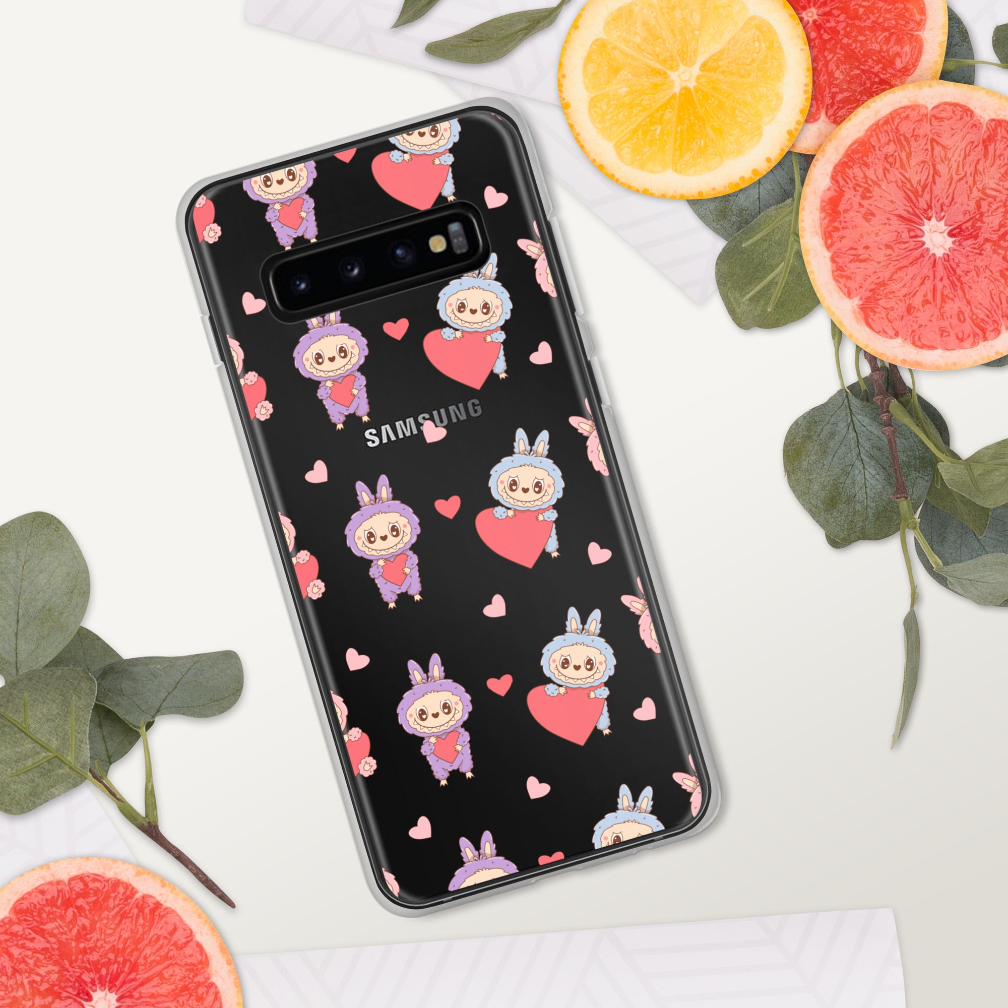 Samsung phone case with cartoon characters and hearts on a black background, surrounded by sliced oranges and grapefruits.