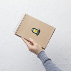Hand holding a brown notebook with a sticker on a light gray textured background