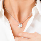 Silver necklace with a heart-shaped pendant worn by a person in a white shirt.