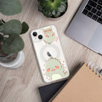 Phone case with a cute green dinosaur design on a wooden surface with plants and a laptop.