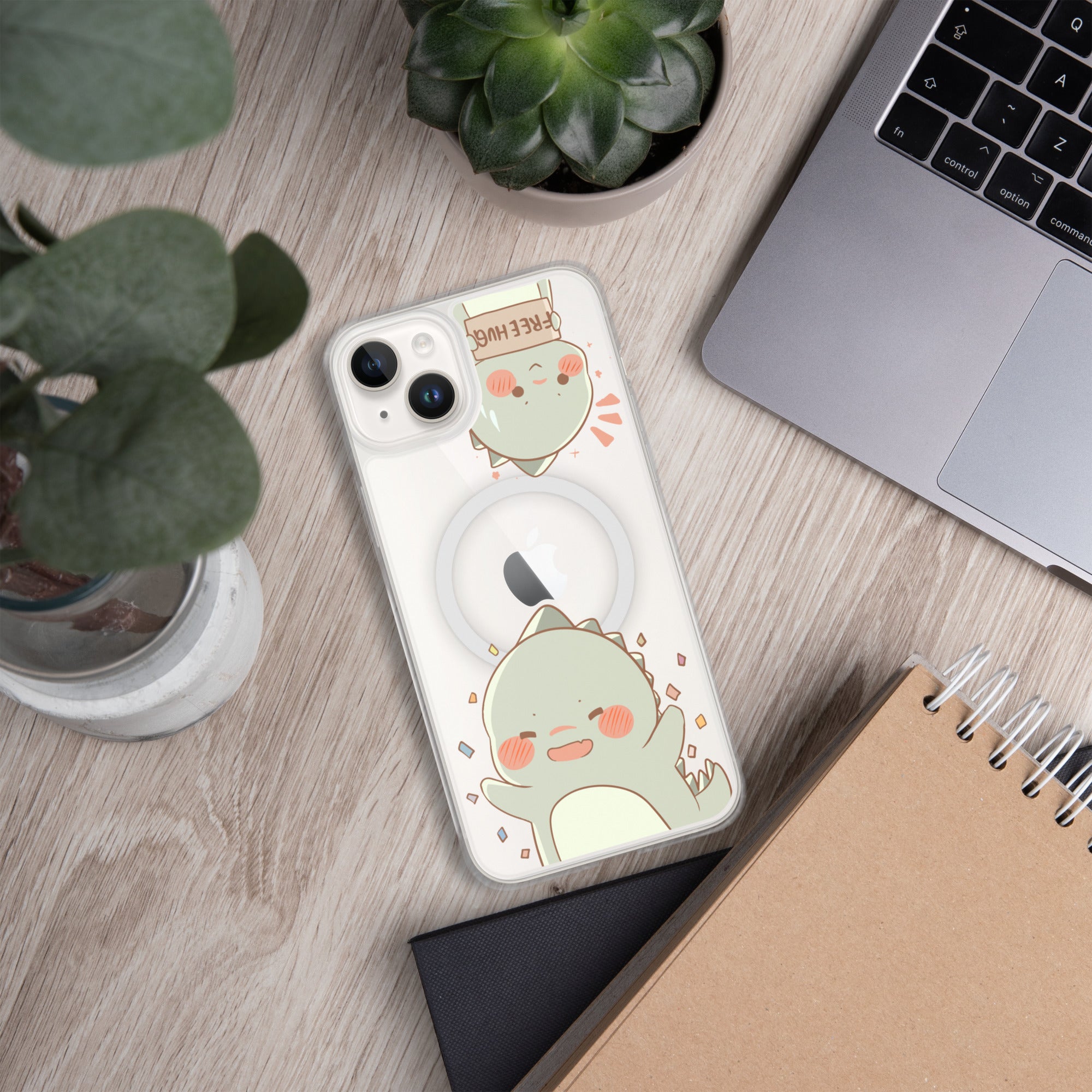 Phone case with a cute green dinosaur design on a wooden surface with plants and a laptop.