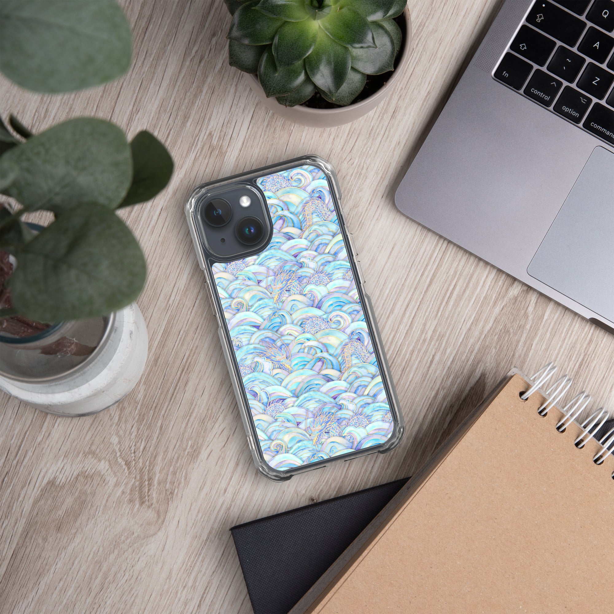 Phone with a colorful case on a desk next to a laptop, notebook, and plants
