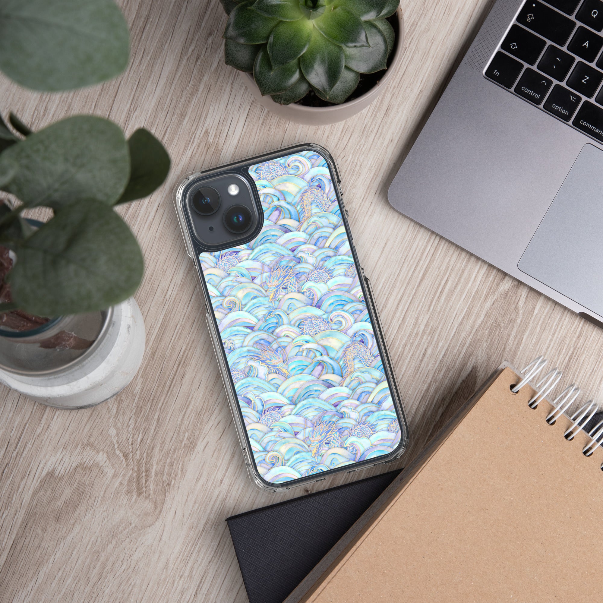 Phone with a colorful case on a desk next to a laptop, plant, and notebook