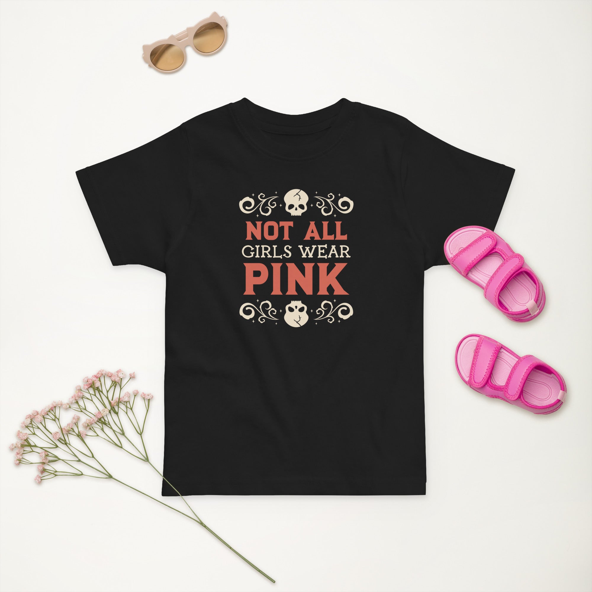 Black t-shirt with 'Not All Girls Wear Pink' text, pink sandals, and dried flowers on a white background