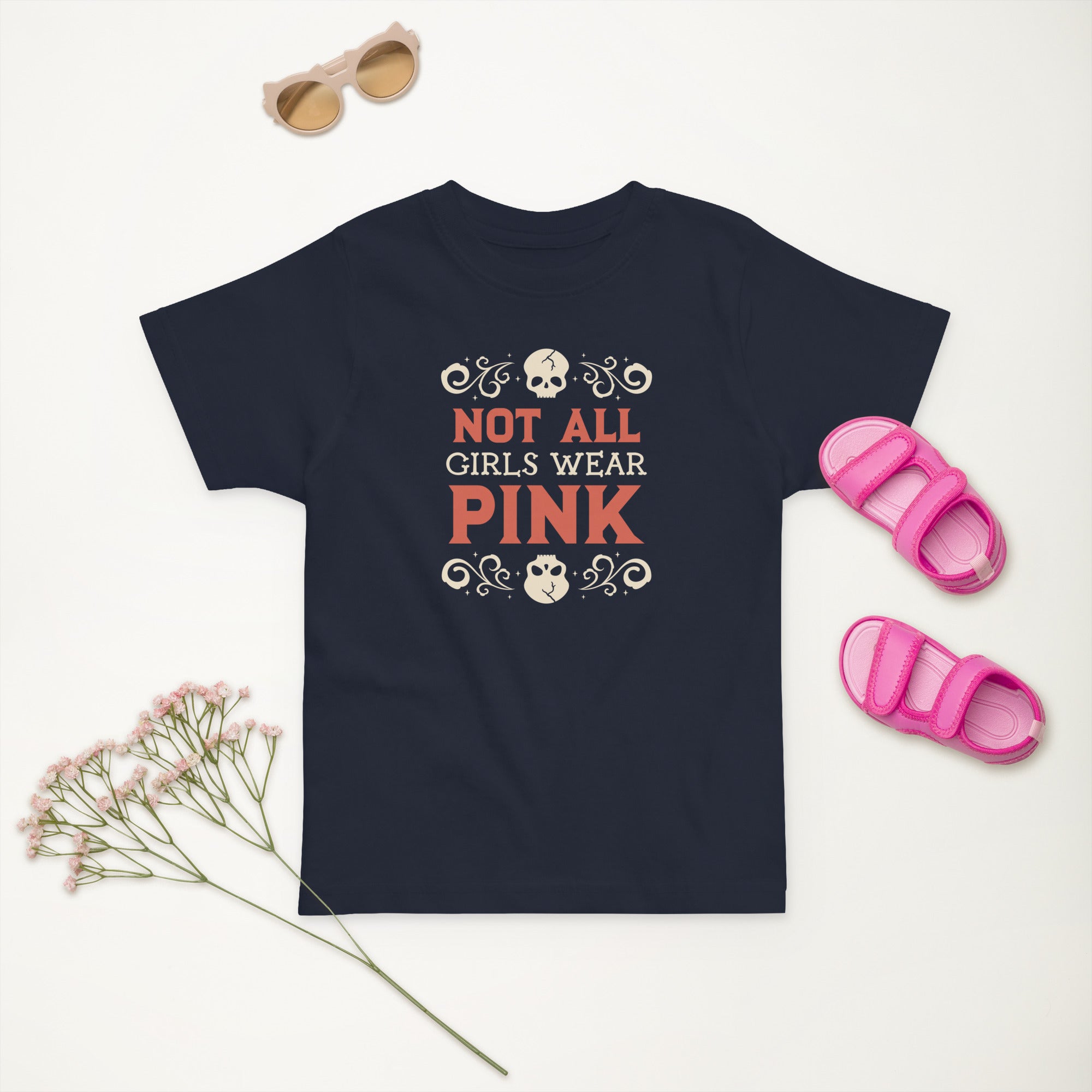 Navy blue t-shirt with 'Not All Girls Wear Pink' text, pink sandals, and sunglasses on a light background